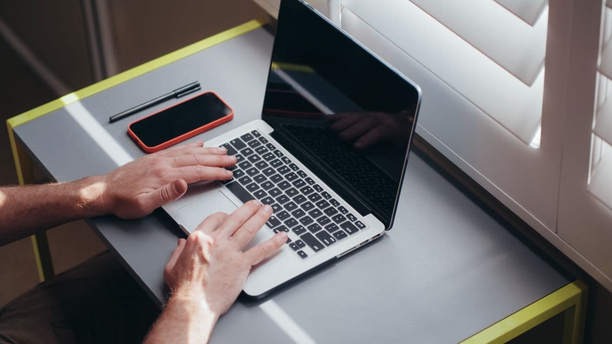 Hands typing a room listing on a laptop at a tidy desk